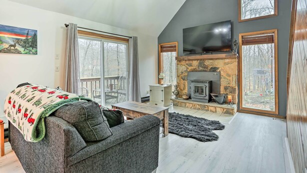 A living room with a fireplace, a television mounted above it, and a large window with curtains. - 4 Mi to Tubing: Cozy Bushkill Cabin w/ Deck! (Bushkill)