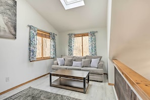 Uma sala de estar com sofá, mesa de centro e duas janelas com cortinas.