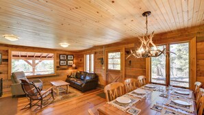 Een houten cabin-interieur met een eettafel voor zes personen, een leren bank en een schommelstoel.
