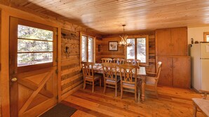 Een houten chalet van binnen, met een eettafel, stoelen, een kroonluchter en een koelkast.