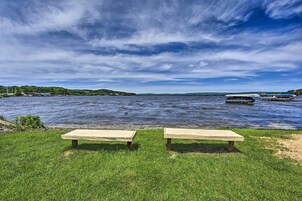 Vista del lago con dos bancos de madera orientados hacia el agua, un bote amarrado a la derecha y una orilla distante con vegetación.