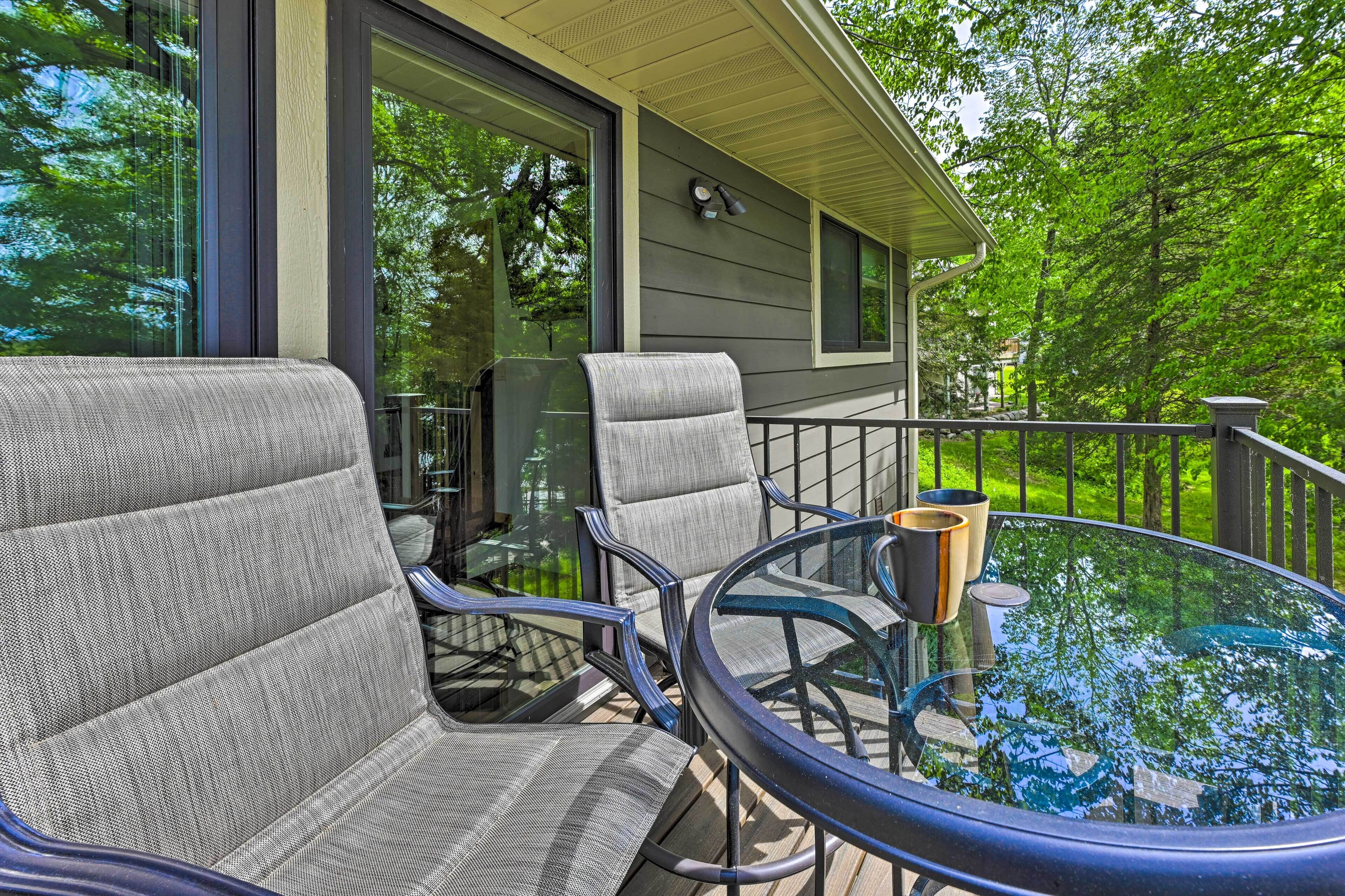 A deck with two chairs and a glass table, overlooking a lush green landscape.