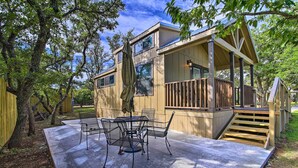 A covered patio with a table and chairs, a wooden deck, and a staircase leading to a second level.