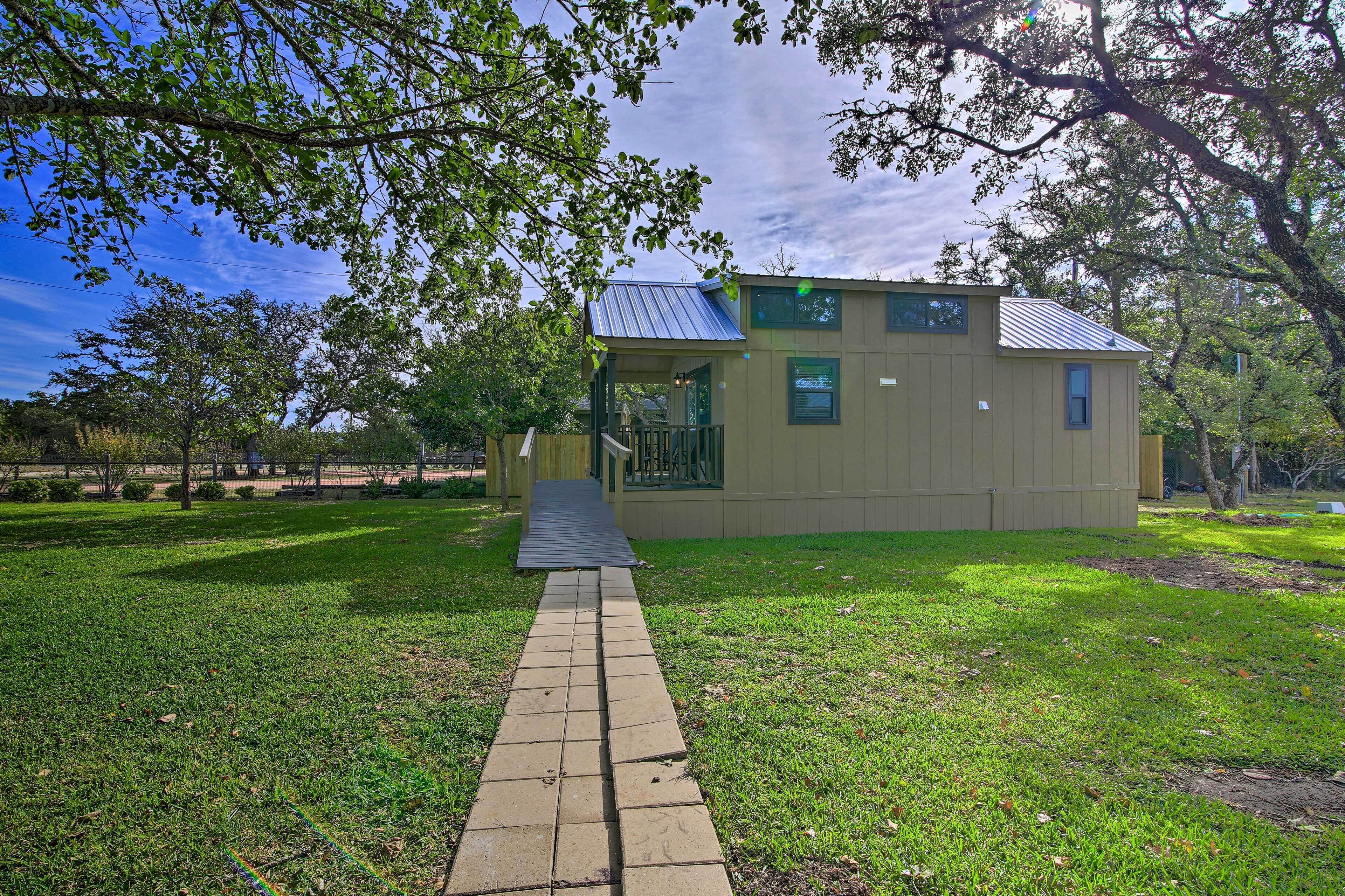 A small, single-story building with a metal roof, a covered porch, and a paved pathway leading to it.