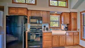 A kitchen with wooden cabinets, a black refrigerator, a microwave, an oven, and a sink.