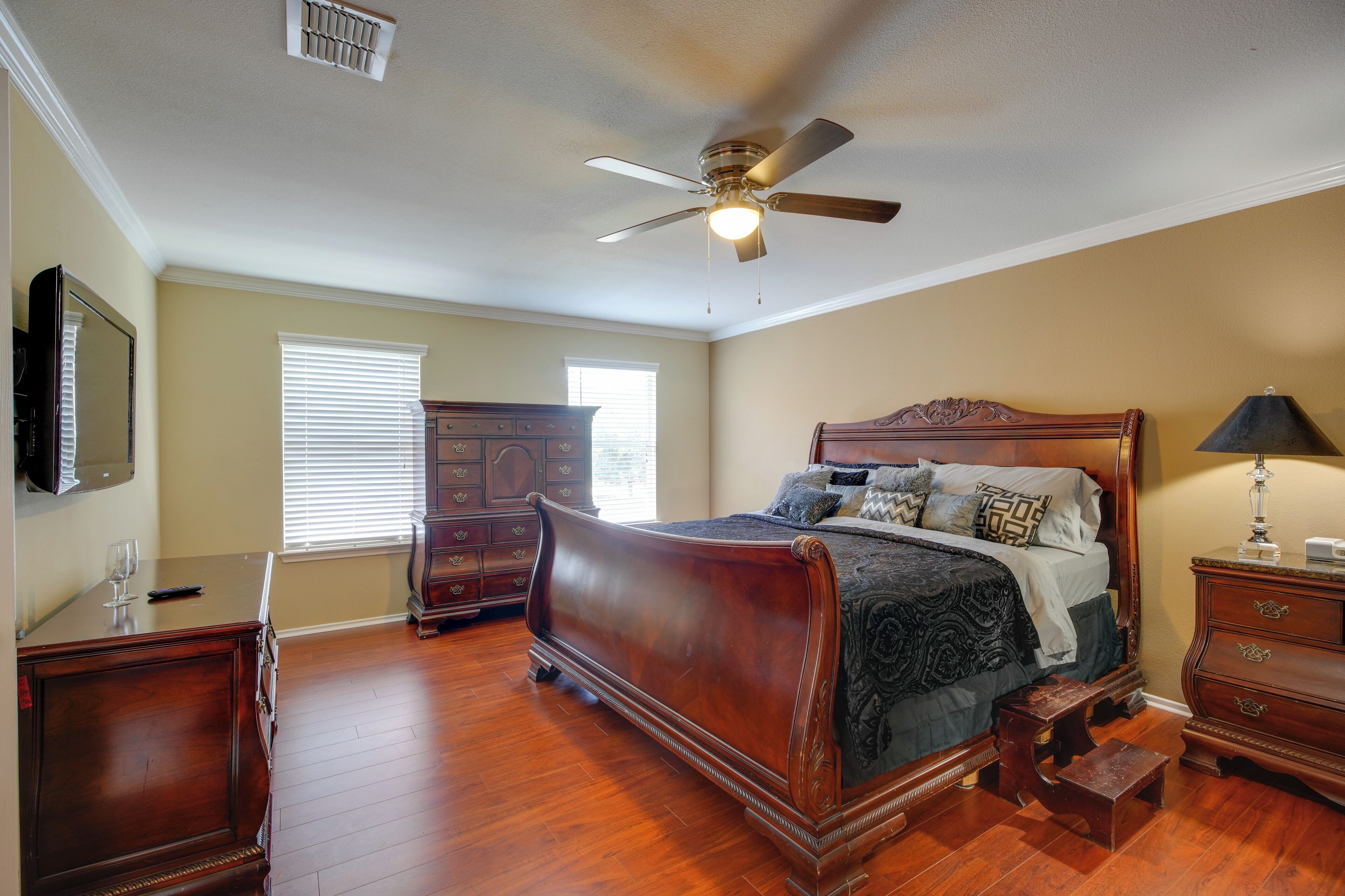 A bedroom with a wooden bed, a ceiling fan, a dresser, and a nightstand.