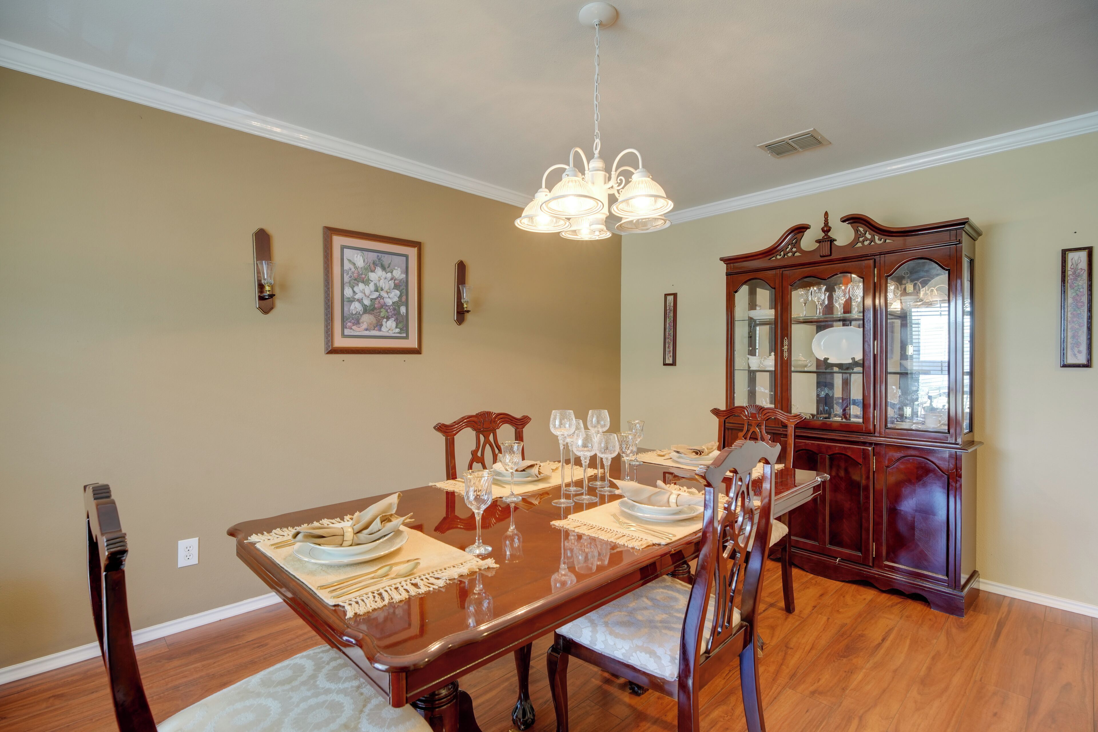 A dining room with a wooden table set for six, surrounded by chairs, a wooden cabinet, and a chandelier.