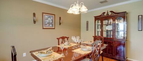 A dining room with a wooden table set for six, surrounded by chairs, a wooden cabinet, and a chandelier.