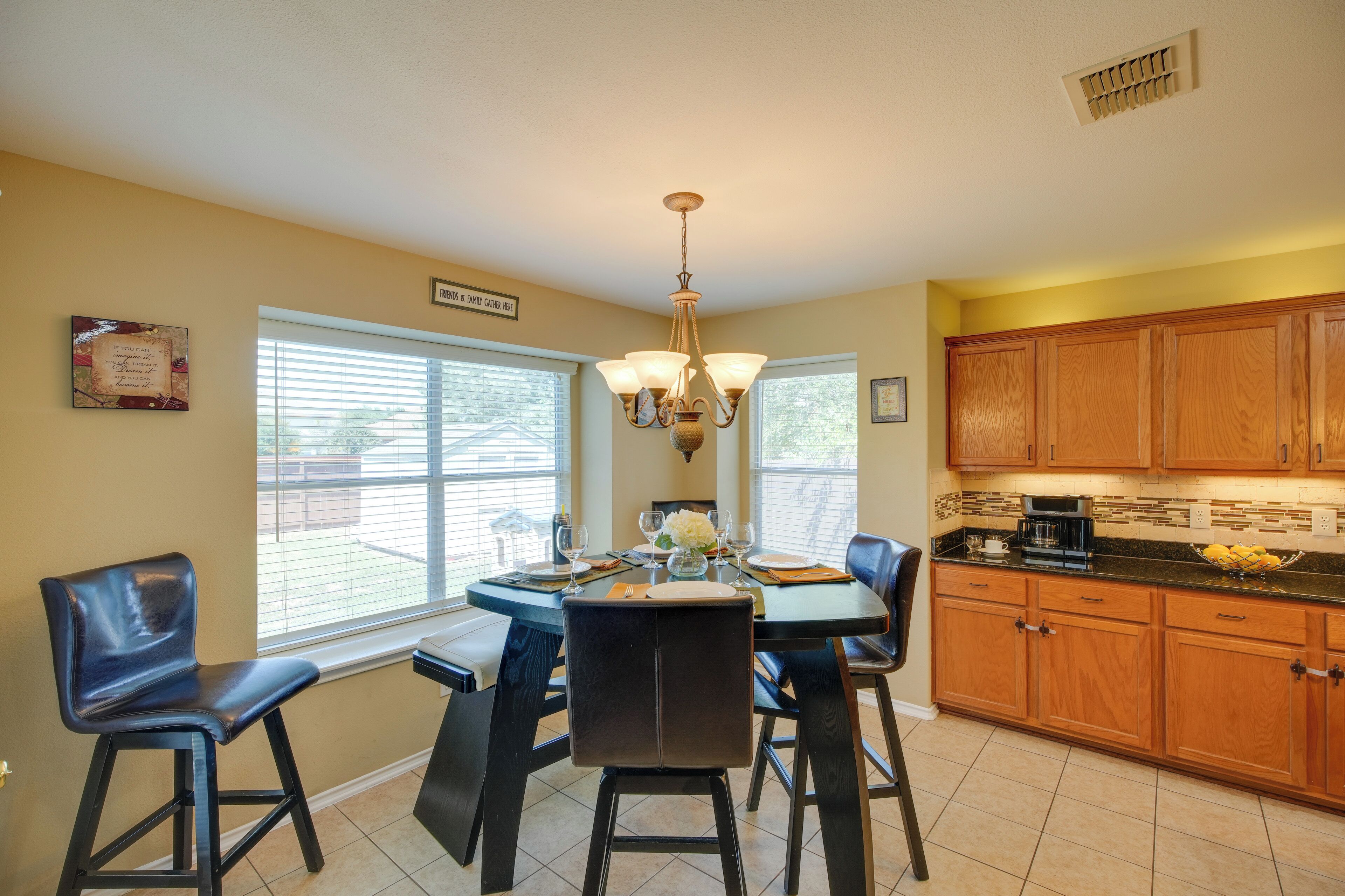 A dining area with a round table, four chairs, a chandelier, and wooden cabinets.