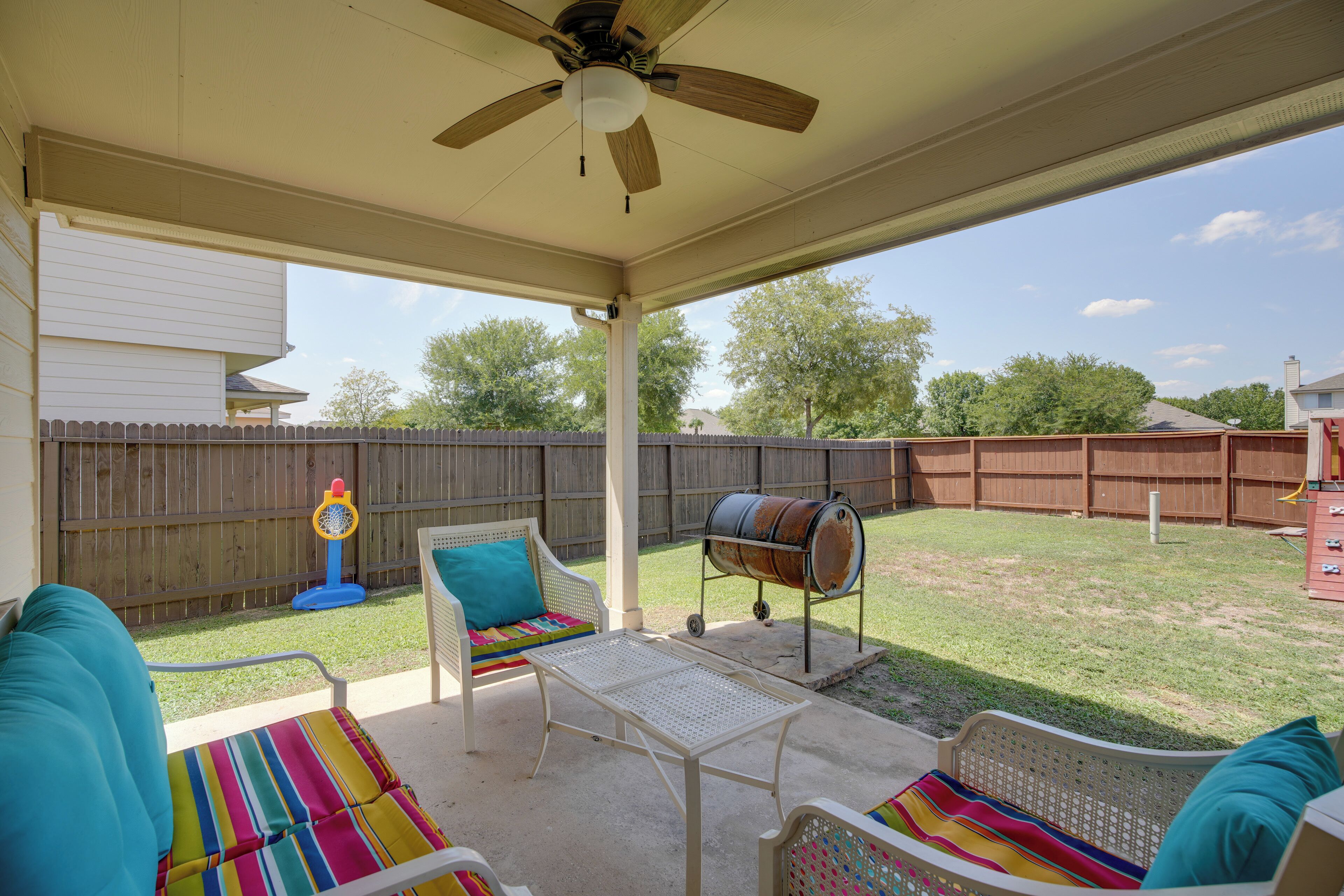 A covered patio with a ceiling fan, a barbecue grill, and outdoor seating with colorful cushions.