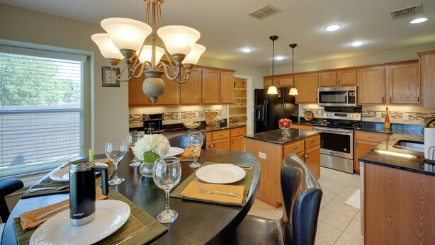A modern kitchen with wooden cabinets, stainless steel appliances, and a dining area with a table set for two. - Near Seaworld! Modern Family Home w/ Pool Access (San Antonio)