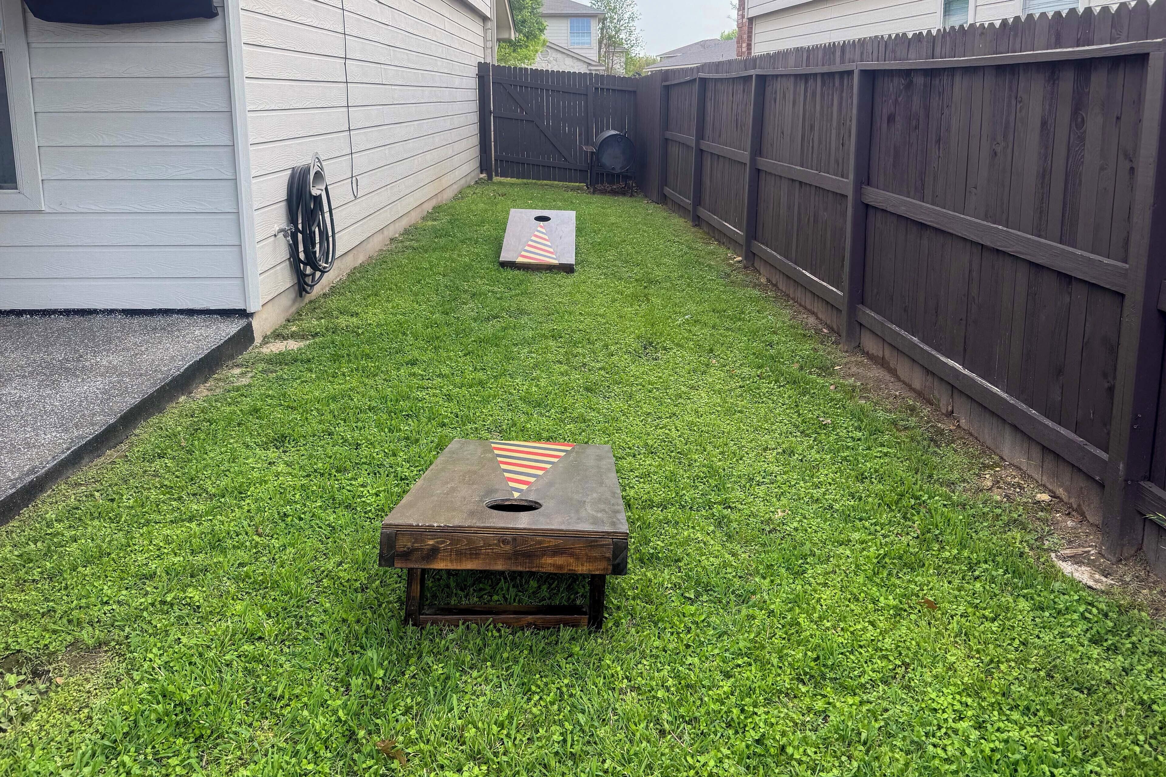 A backyard with a wooden table and a game board, surrounded by a wooden fence and a house.