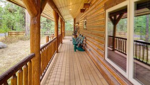 A wooden deck with benches, large windows, and a view of the surrounding forest. - Exquisite Mccall Log Cabin - Walk to Payette Lake! (McCall)