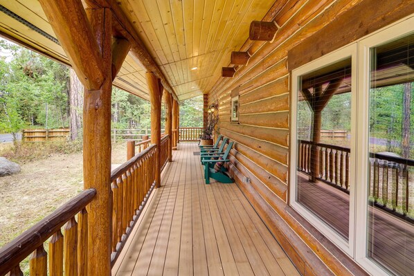 A wooden deck with benches, large windows, and a view of the surrounding forest.