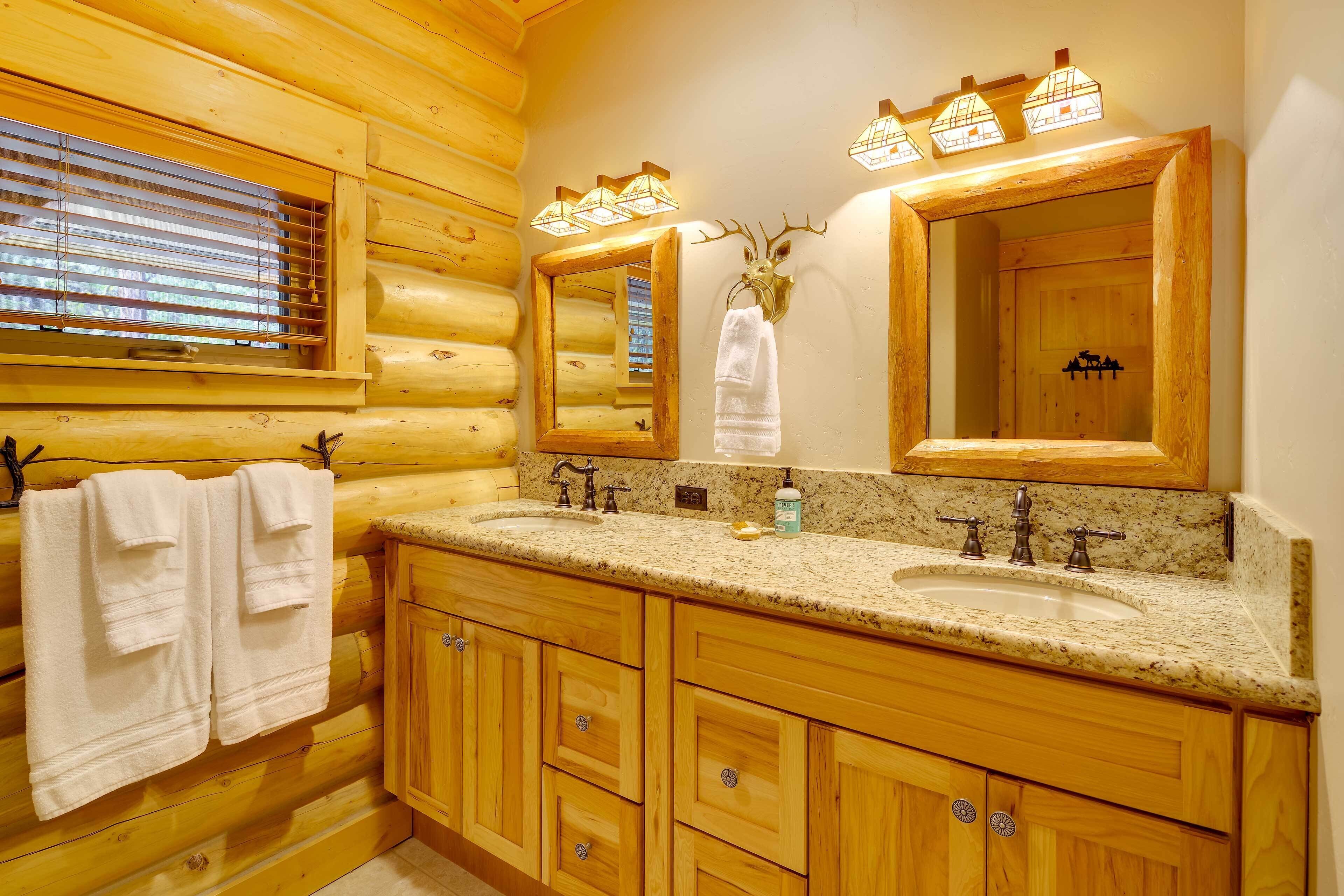 A wooden cabin-style bathroom with two sinks, wooden cabinets, a mirror, and a deer head mounted on the wall.