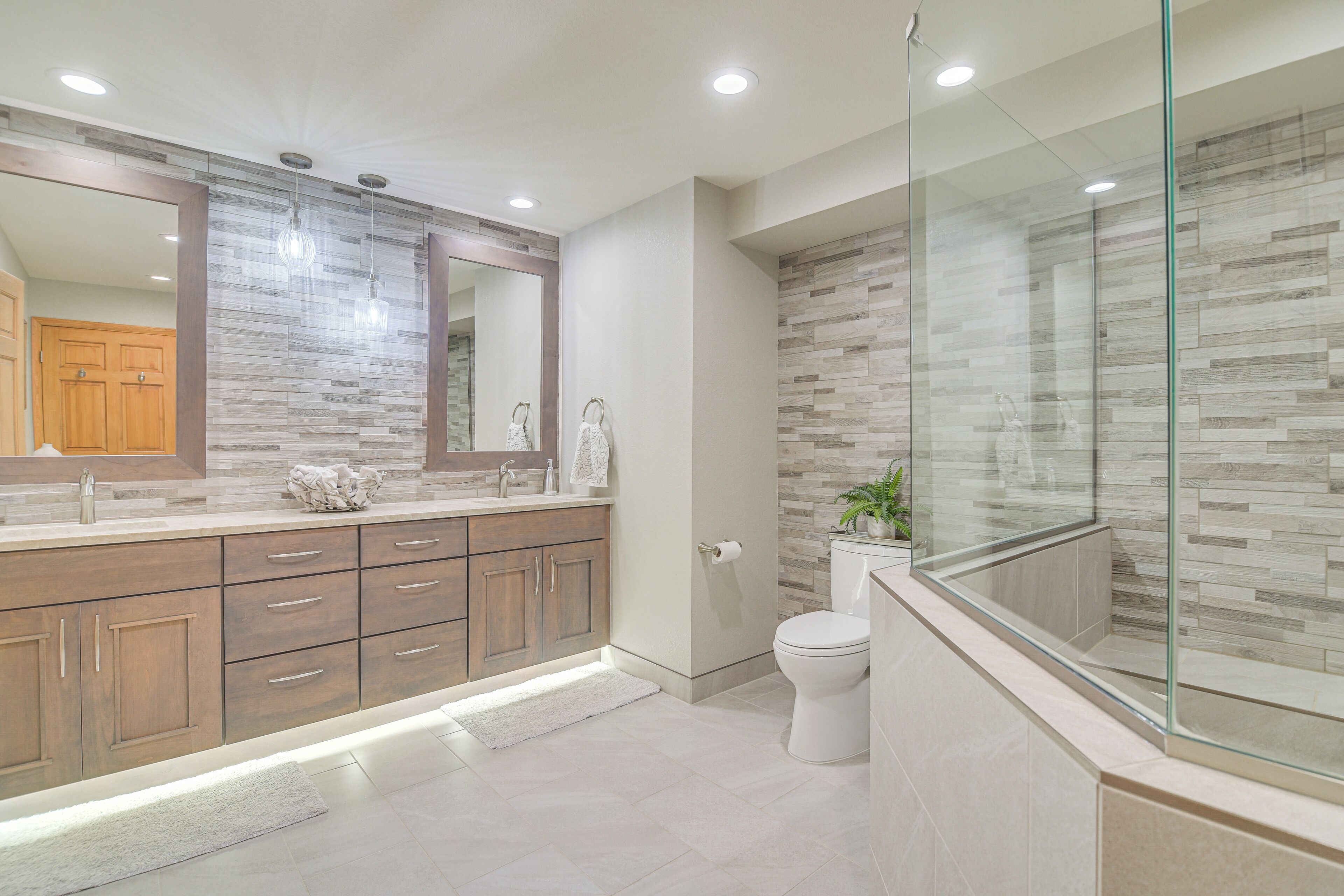 Un baño moderno con un espejo grande, armarios de madera, una mampara de vidrio y un inodoro.