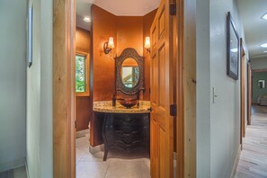 Un pasillo con una puerta de madera, un espejo y un lavabo con un recipiente de cobre.