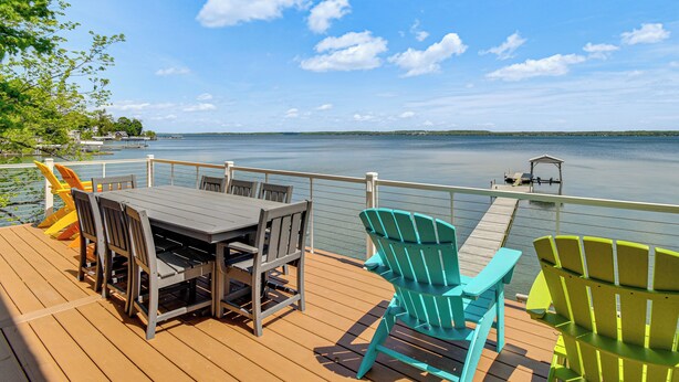 Une terrasse en bois avec une table et des chaises, donnant sur un lac paisible.