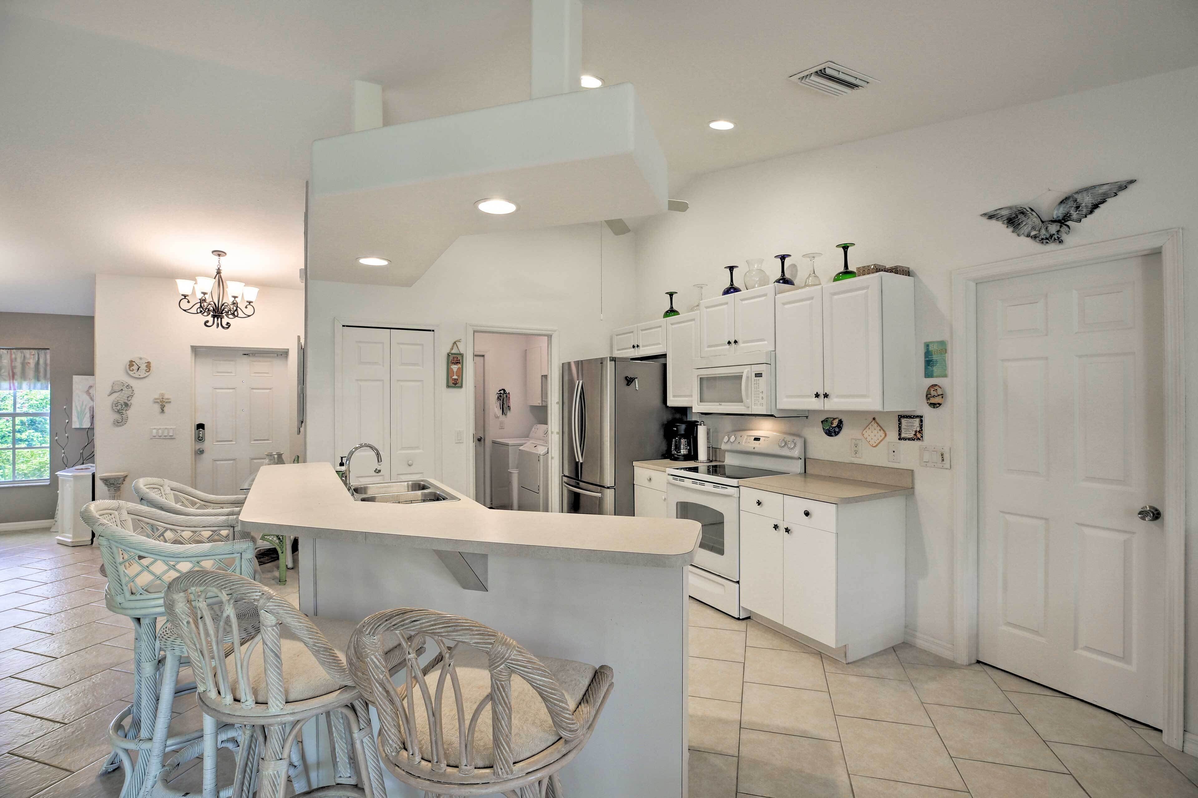 A modern kitchen with white cabinetry, a central island, wicker chairs, and a chandelier.