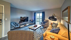 A living room with a sofa, armchair, and a coffee table. There is a television and a lamp.