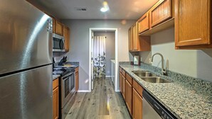 A kitchen with stainless steel appliances, wooden cabinets, granite countertops, and a dishwasher.