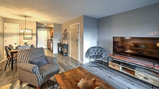 A modern living room with a flat-screen TV, a striped sofa, a leather armchair, and a wooden coffee table.