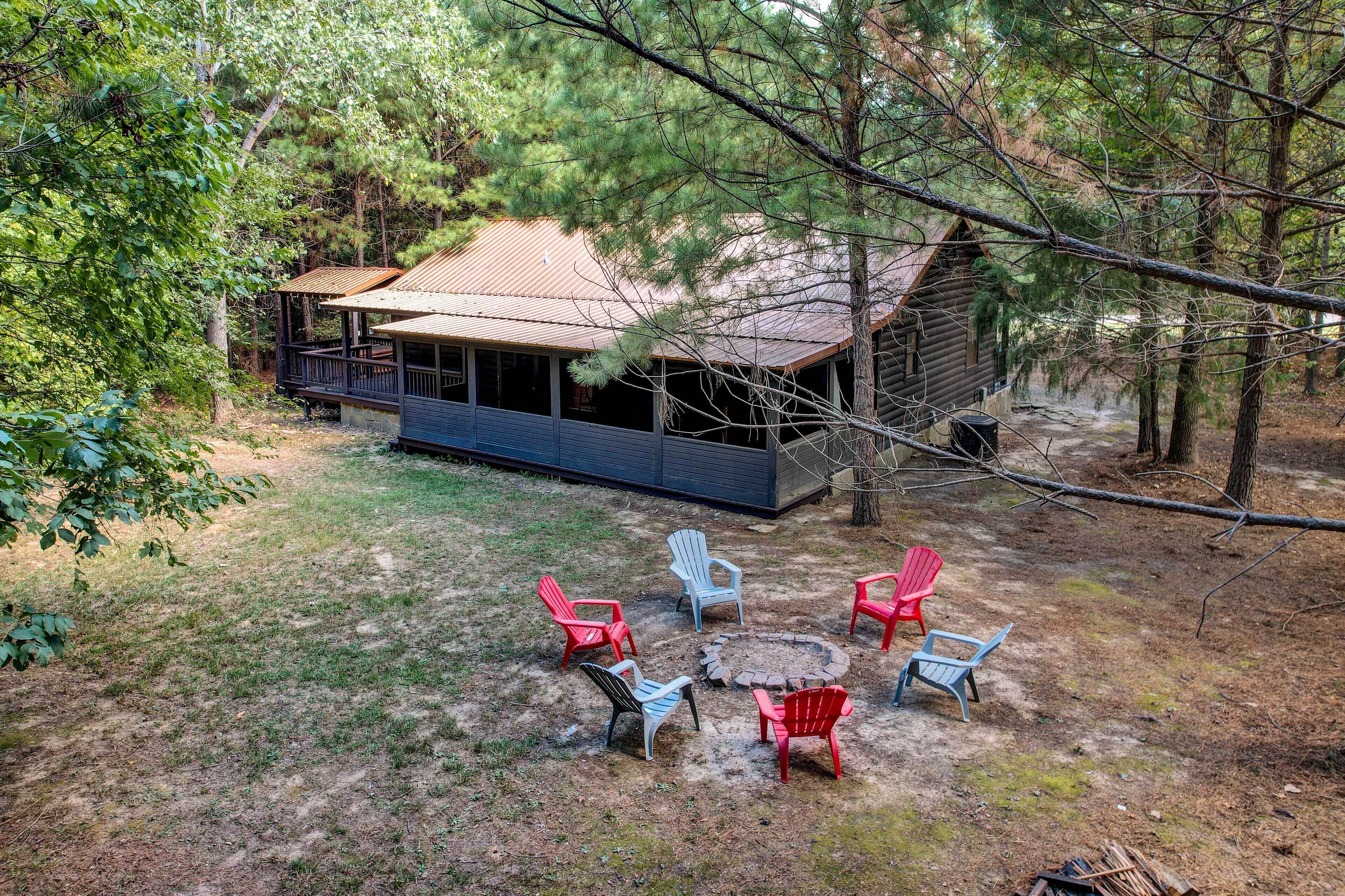 A cabin with a porch and a fire pit surrounded by Adirondack chairs.