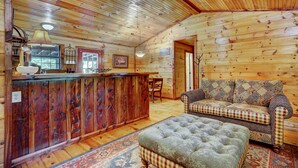 L’intérieur d’un chalet en bois comprend un coin bar, un canapé à motifs et un pouf capitonné.