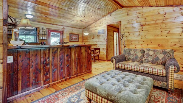 A wooden cabin interior with a bar area, a patterned sofa, and a tufted ottoman. - Private Broken Bow Cabin w/ Hot Tub + Gazebo! (Broken Bow)