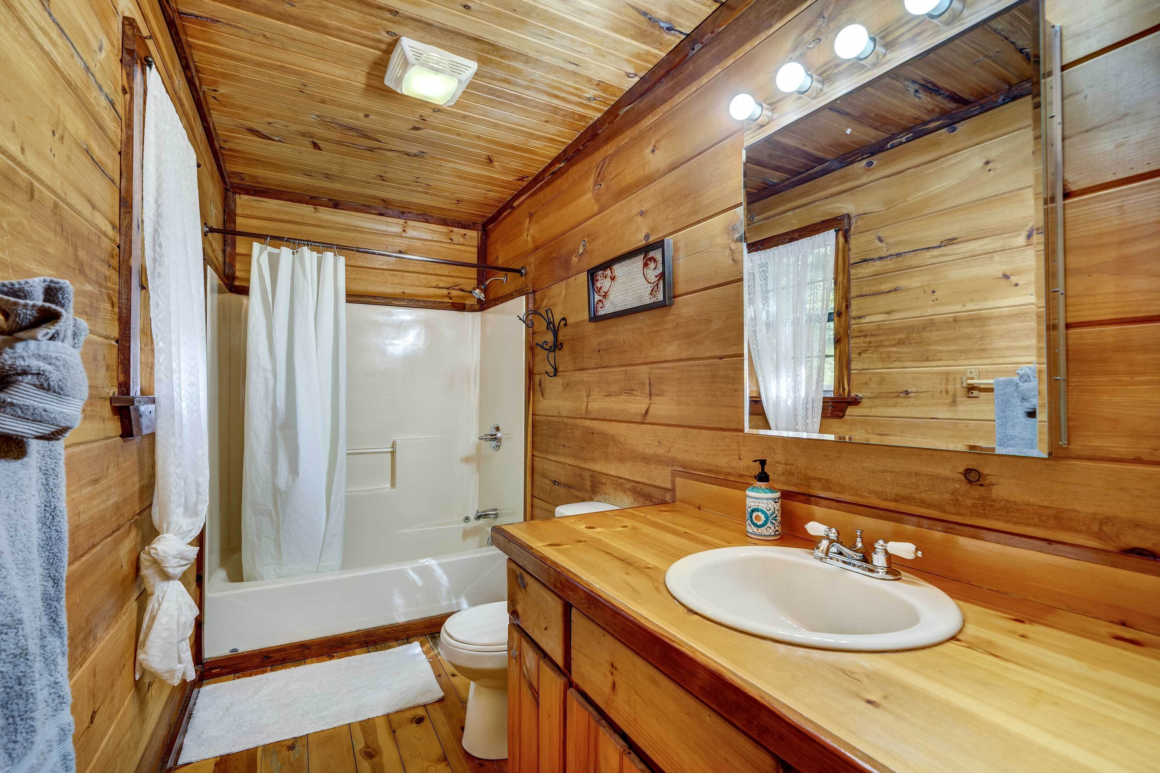 Un baño de cabaña de madera con bañera, inodoro, lavamanos y un espejo grande.