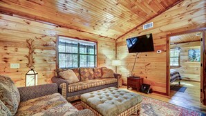 A cozy log cabin interior with a sofa, ottoman, and a television mounted on the wall. - Private Broken Bow Cabin w/ Hot Tub + Gazebo! (Broken Bow)