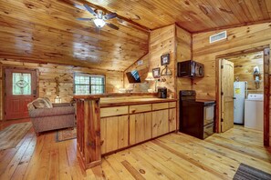 A cabin interior with a wooden ceiling, a ceiling fan, a kitchen area with a stove and refrigerator, and a seating area with a sofa. - Private Broken Bow Cabin w/ Hot Tub + Gazebo! (Broken Bow)