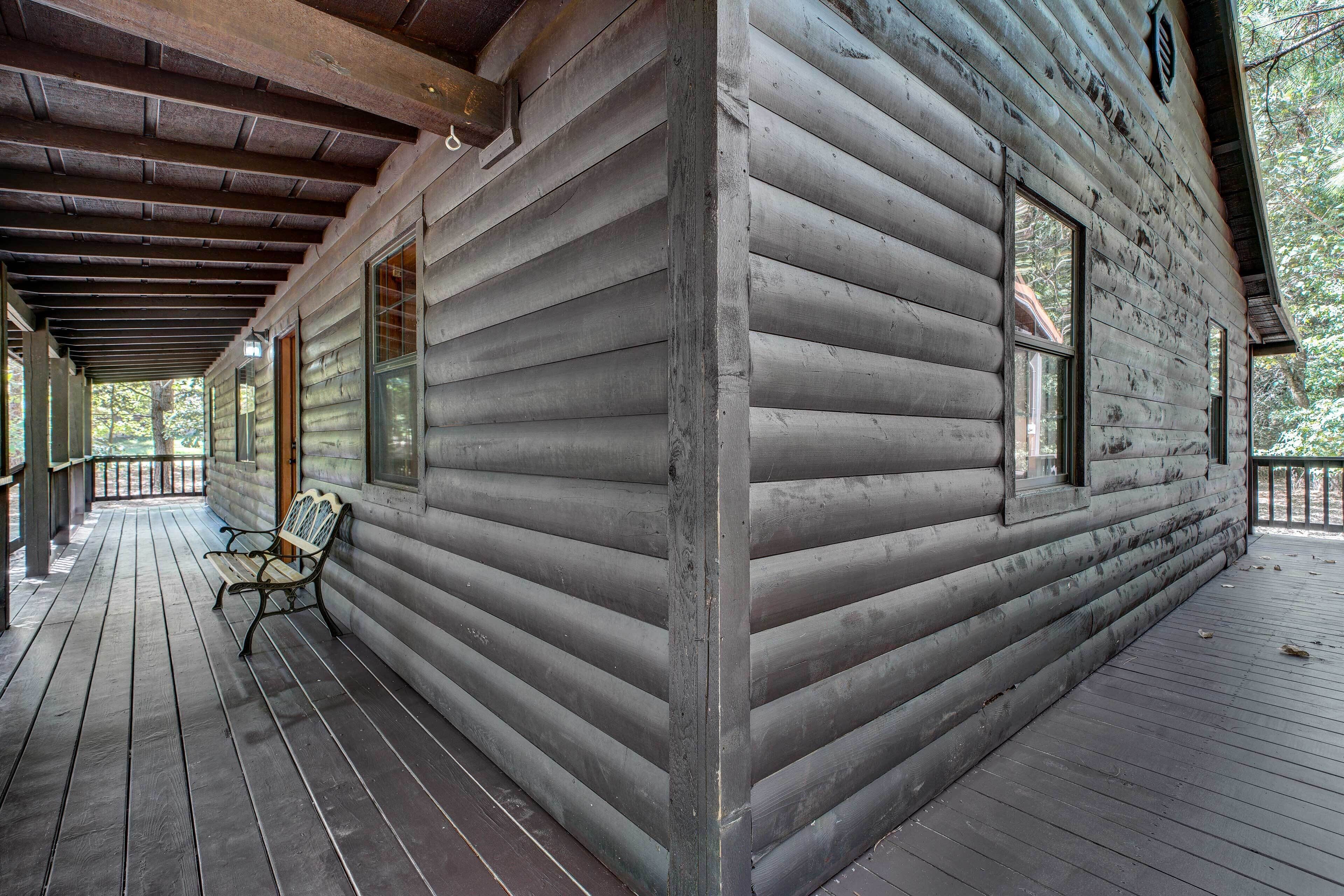 A log cabin with a wooden deck, a bench, and large windows.