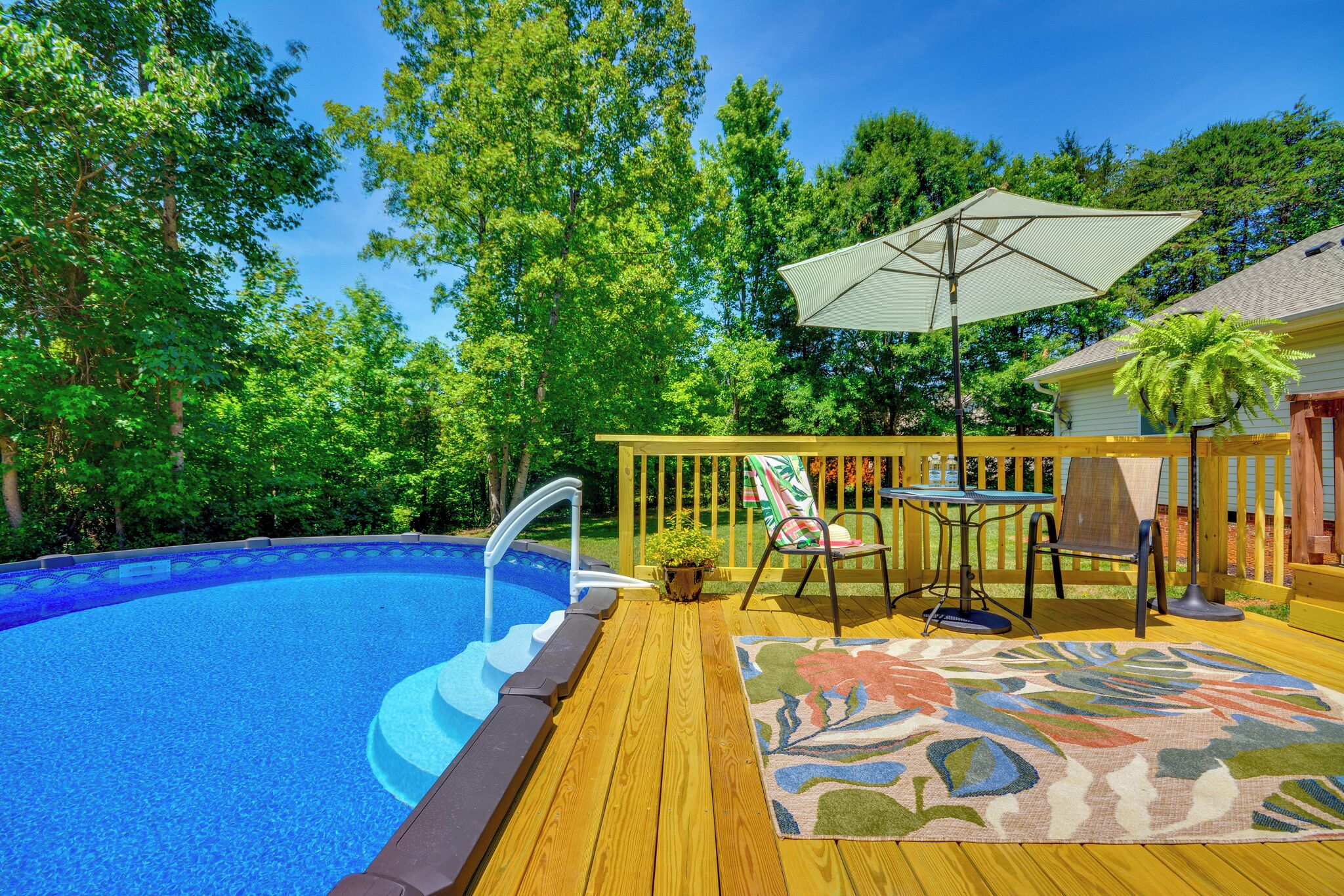A swimming pool with a wooden deck, a lounge chair, a table, and an umbrella.