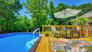 A swimming pool with a wooden deck, a lounge chair, a table, and an umbrella.