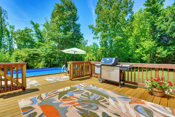 A wooden deck with a grill, a pool, and a wooden fence.