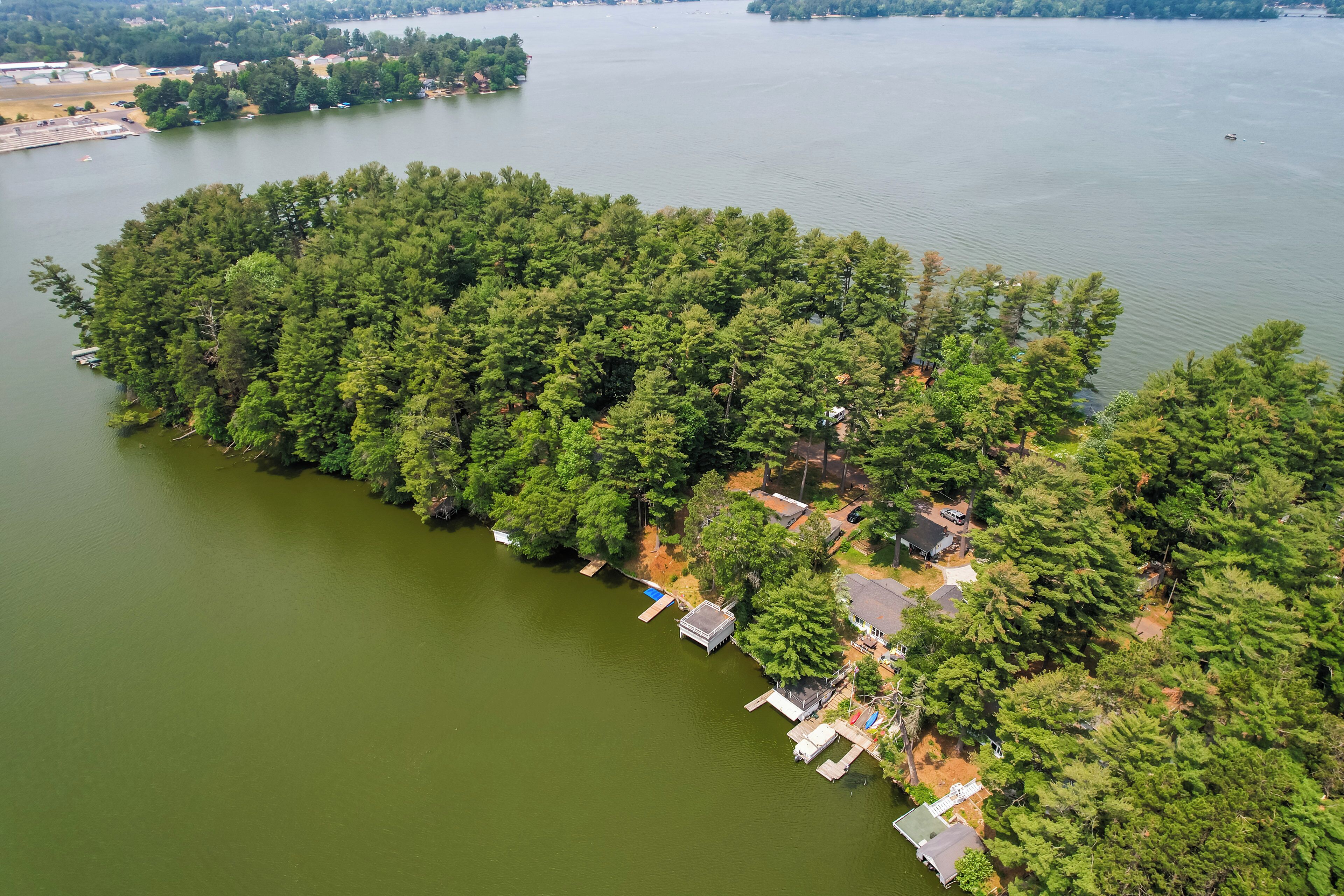 An aerial view of a lakeside property with dense forest, docks, and small buildings.