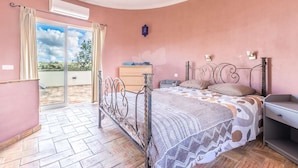 A bedroom with a bed, a dresser, and a nightstand. There is a window with curtains and an air conditioning unit on the wall. - Beautiful villa with private pool and sea view (foupana, moncarapacho)