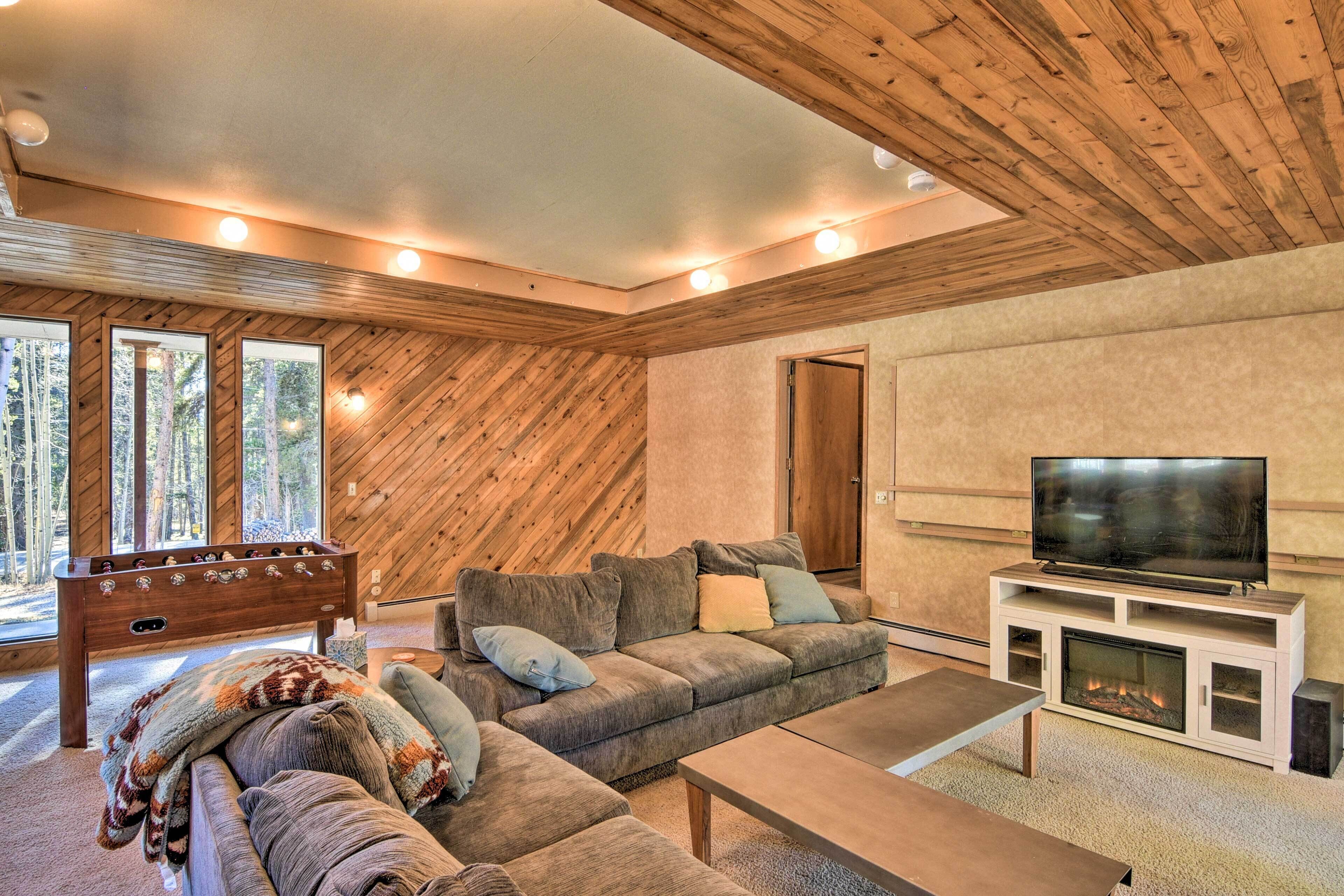 A cozy living room with a wooden ceiling, a large sofa, a television, and a fireplace.