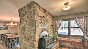 A stone fireplace with a pizza oven, a dining area with wooden chairs, and a large window with curtains. - Charming Leadville Retreat w/ Private Hot Tub (Leadville)
