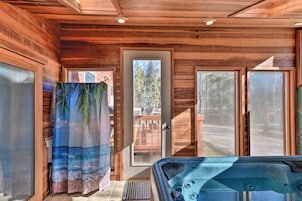 Una cabaña de madera con jacuzzi, ventanas amplias y puerta que da al exterior.