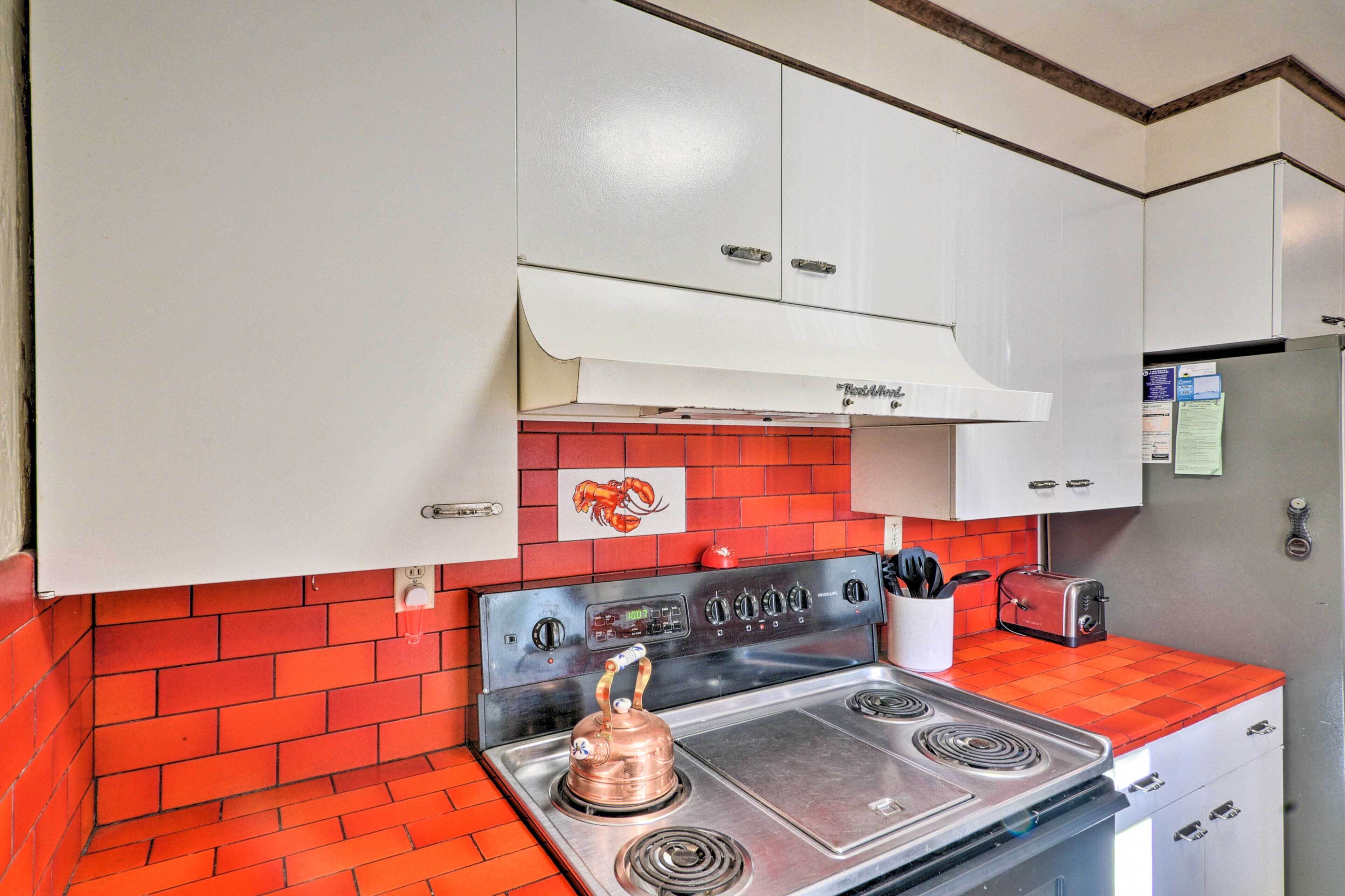 A kitchen with a red tiled backsplash, stainless steel appliances, white cabinets, and a red toaster.