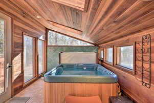 Interior de una cabaña de madera con jacuzzi, ventanas amplias y techo de madera.