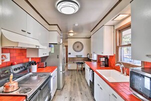 Cocina compacta con estufa, lavamanos y refrigerador, con piso de madera y detalles en rojo.