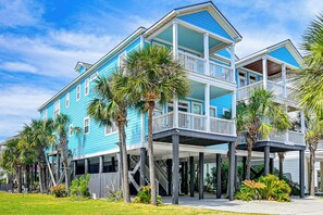 A two-story beachfront house with a balcony, palm trees, and a clear sky. - Luxury Home w/ Ocean View, Private Pool, & Hot Tub (Murrells Inlet)