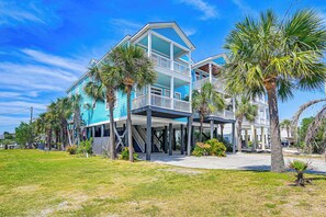 A two-story beachfront house with a balcony, palm trees, and a clear blue sky. - Luxury Home w/ Ocean View, Private Pool, & Hot Tub (Murrells Inlet)
