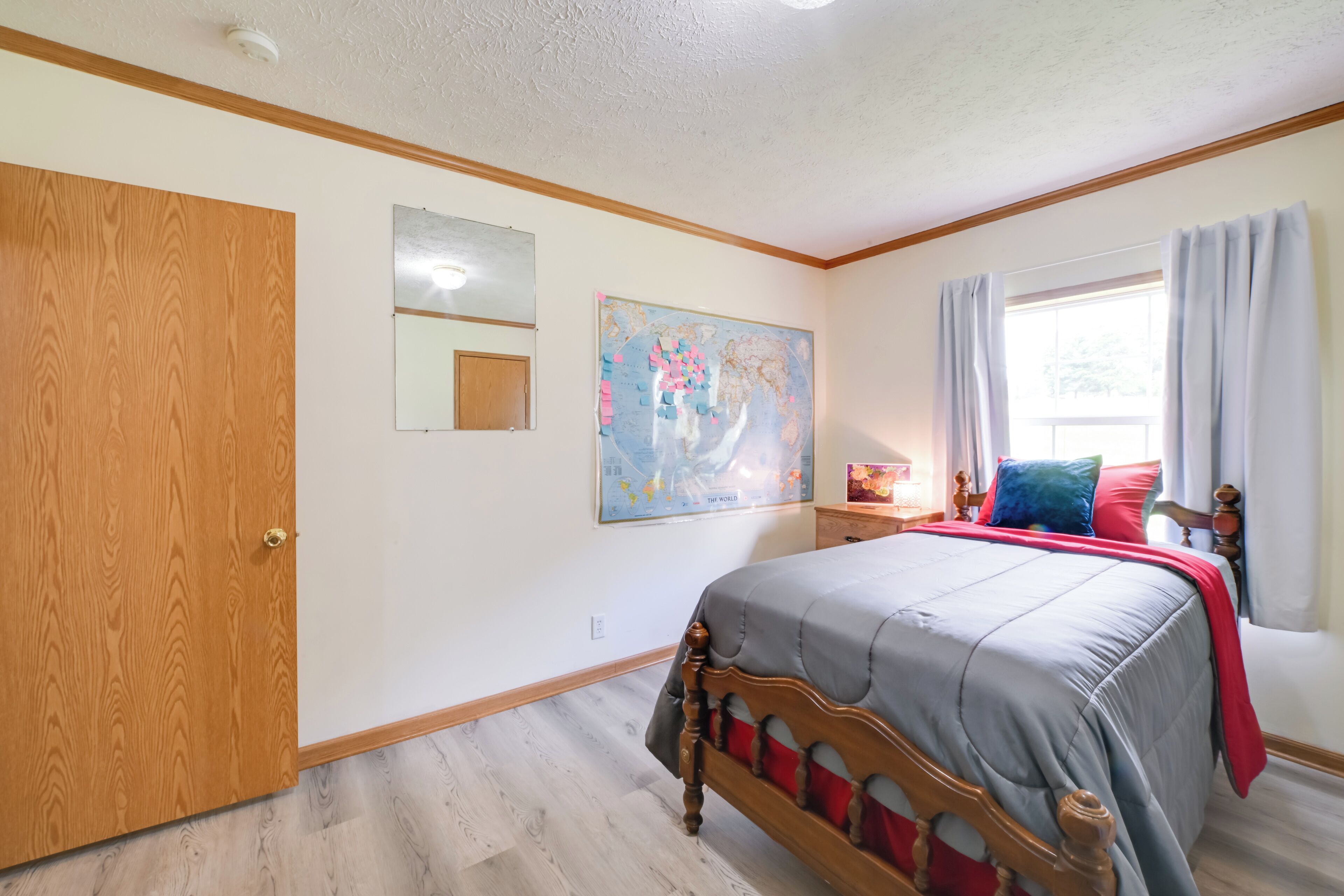 A bedroom with a wooden bed, a map on the wall, a window with curtains, and a wooden door.