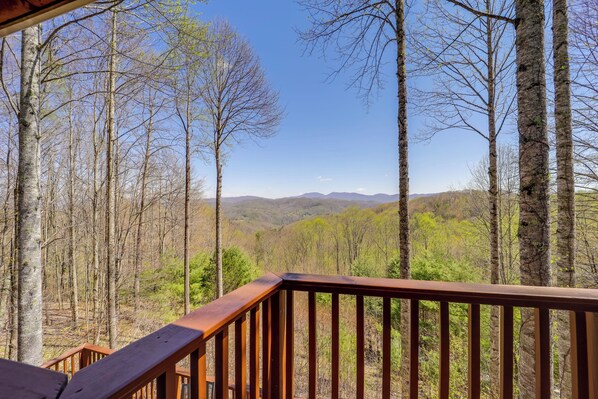 Una terraza de madera con vista a un bosque y montañas distantes.