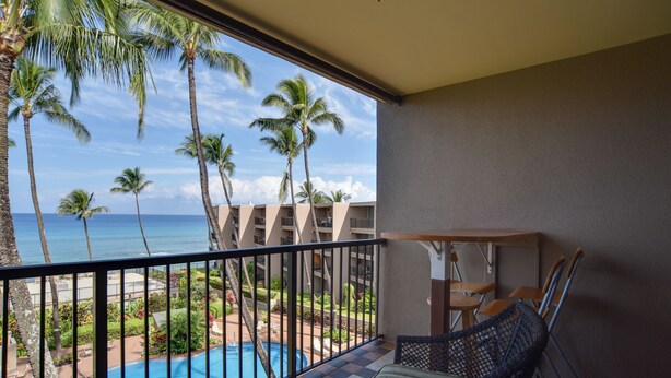A balcony with a view of a pool, palm trees, and a building with multiple floors. - Oceanfront Lahaina Condo w/ Balcony & Pool Access! (Napili-Honokowai)