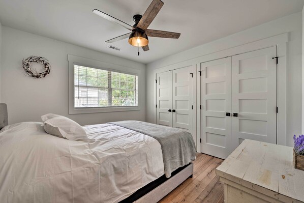 A bedroom with a bed, a ceiling fan, a window, and white doors.